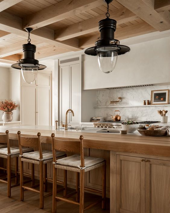 a beautiful earthy kitchen with white cabinets and a built in hood, a large stained kitchen island, vintage pendant laps