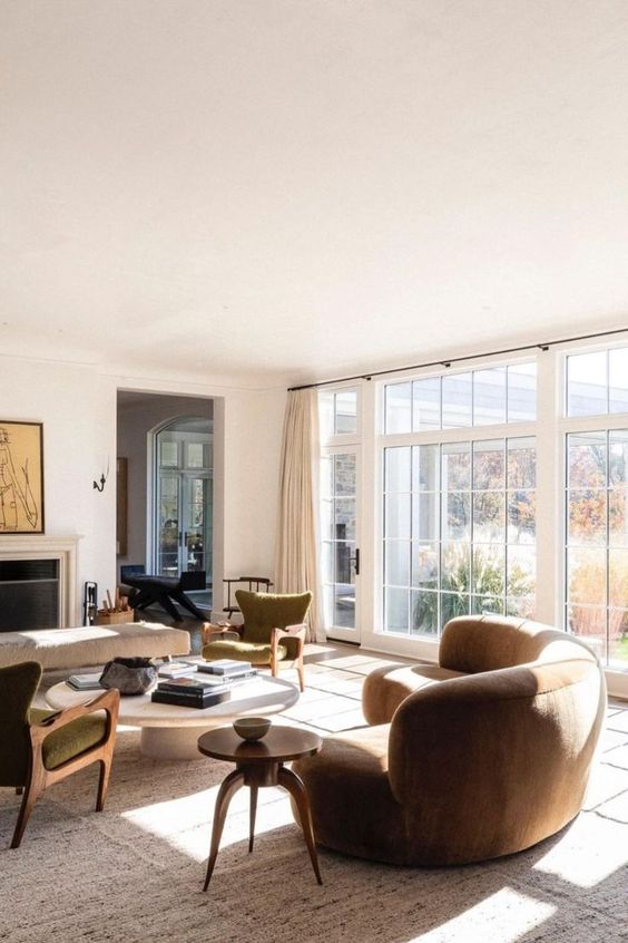 a beautiful earthy living room with a fireplace, green chairs, a rust-colored curved sofa, a low coffee table and a bench