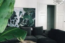 a beautiful eclectic living room with a black velvet sectional, a tree slice coffee table, a tropical print, a crystla chandelier and a statement plant