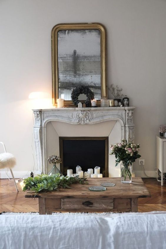a beautiful living room with a French fireplace, a stained wood coffee table, a white sofa, a mirror in a shiny frame and candles