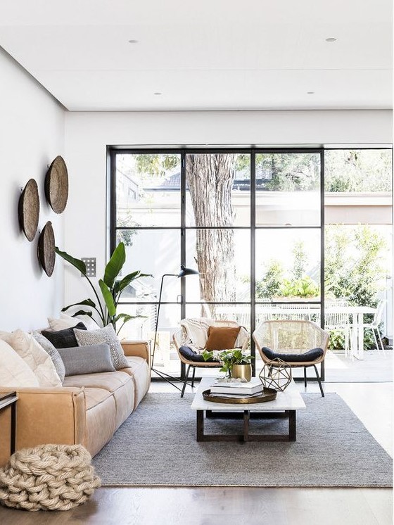 a beautiful living room with a glazed wall, a low leather sofa, a low coffee table, rattan chairs and potted plants