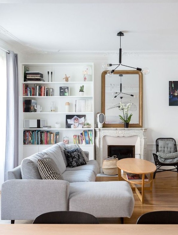a beautiful modern French style living room with a French marble fireplace, a bookcase, a grey sectional, a coffee table and cool lamps