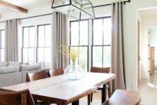 a beautiful modern farmhouse open layout with black frame double-hung windows, grey seating furniture, a living edge table and a bench