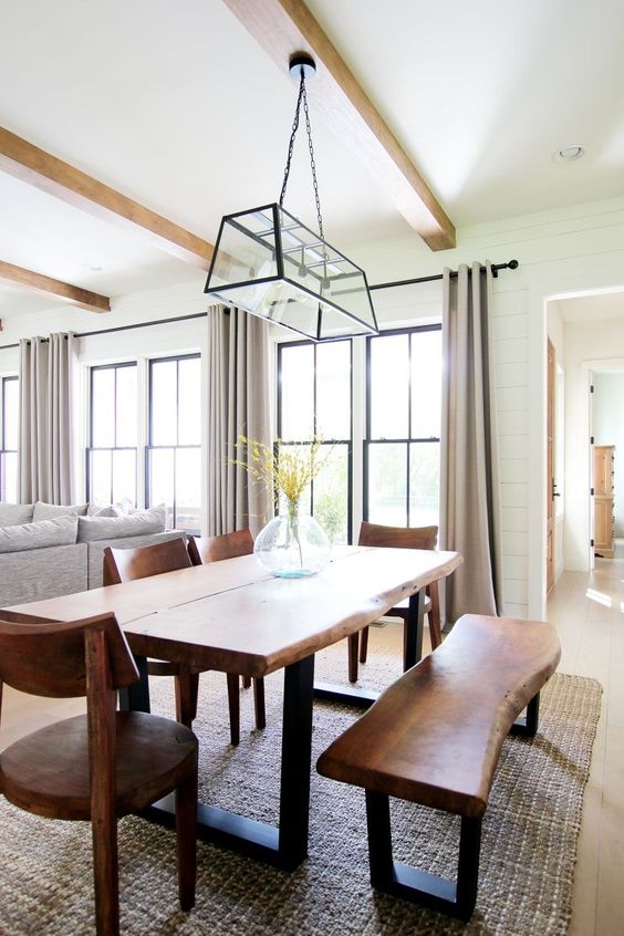 a beautiful modern farmhouse open layout with black frame double-hung windows, grey seating furniture, a living edge table and a bench