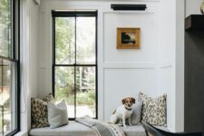 a beautiful neutral modern space with trim on the walls, two black double-hung windows, a built-in windowsill daybed and printed pillows