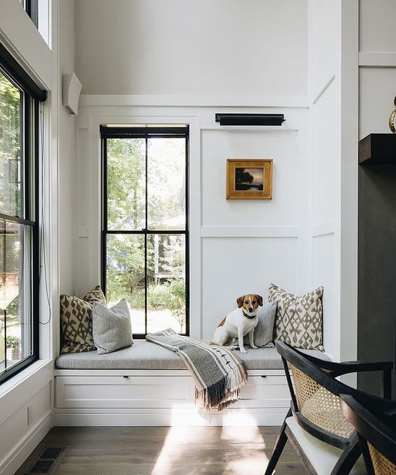 a beautiful neutral modern space with trim on the walls, two black double-hung windows, a built-in windowsill daybed and printed pillows