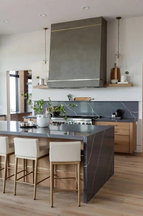 a beautiful stained kitchen with flat panel cabinets, black soapstone countertops and a backspalsh, a grey hood and pendant lamps