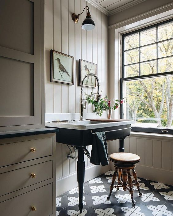 a beautiful vintage space with tan beadboard and cabinetry, black and white tiles, a black French double hung window, a sink on a black stand