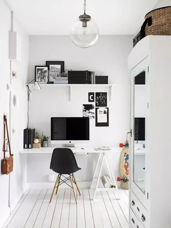 a black and white Scandinavian home office with a white trestle desk, a black Eames chair, a white shelf and black decor, a glass pendant lamp