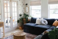 a boho living room with a black sectional, a woven pouf and a planter with greenery, an accent wall and a printed boho rug