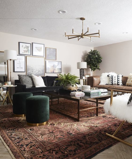 a boho living room with a black sofa, a low coffee table, a brown leather sofa, a boho printed rug and green poufs