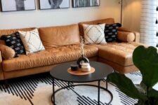a boho living room with an amber leather sofa, a gallery wall, a black table, a printed rug and some decor
