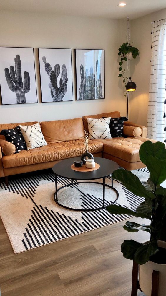 a boho living room with an amber leather sofa, a gallery wall, a black table, a printed rug and some decor