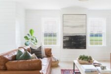 a boho living room with an amber leather sofa, a large coffee table, layered rugs, potted greenery and a big scale artwork