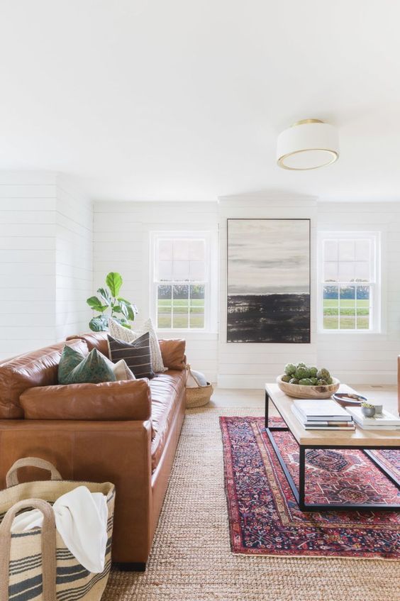 a boho living room with an amber leather sofa, a large coffee table, layered rugs, potted greenery and a big scale artwork