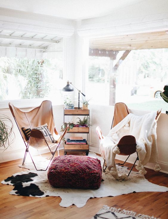 a boho nook with amber leather butterfly chairs, an IKEA cart, a lamp, potted plants, a cowhide rug and a pouf