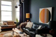 a bold and catchy living room with a black accent wall, a black leather sofa, an amber one, a living edge table, a bulb chandelier