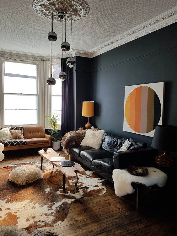 a bold and catchy living room with a black accent wall, a black leather sofa, an amber one, a living edge table, a bulb chandelier