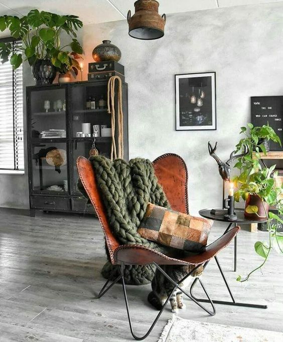 a bold and catchy space with a brown leather butterfly chair, a green chunky blanket, a black display unit and a side table with greenery