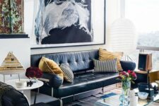 a bold living room with a black leather sofa and a chair, a side table and an acrylic coffee one, a bold print on the wall