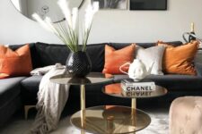 a bold living room with a black sectional, orange pillows, a three-tier coffee table, a mirror and some black and white prints on the wall