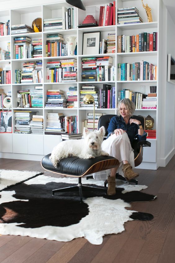 a bold space with an oversized bookcase, a black Eames lounger and an ottoman, a cowhide rug is a cool nook