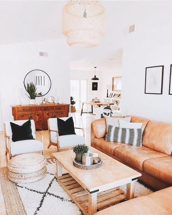 a bright boho living room with an amber leather sofa, a low coffee table, creamy chairs, jute poufs and potted plants