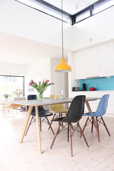 a bright dining space with a white dining table, colorful Eames chairs and a yellow pendant lamp is all cool