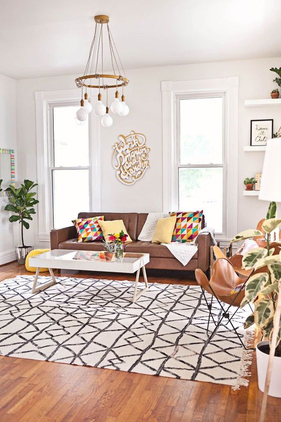 a bright living room with a brown sofa, butterfly chairs, a catchy coffee table, bright printed textiles and a chandelier