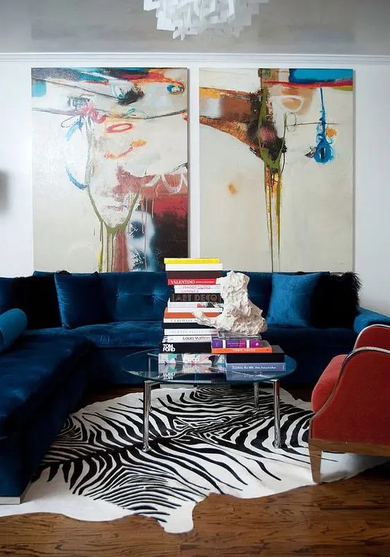 a bright living room with a navy sectional, a red chair, a clear glass coffee table, bold artwork and a zebra print rug is amazing