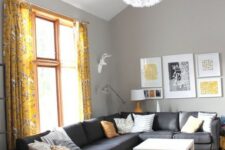 a bright living room with grey walls, a black sectional, a mustard rug and floral curtains plus a gallery wall