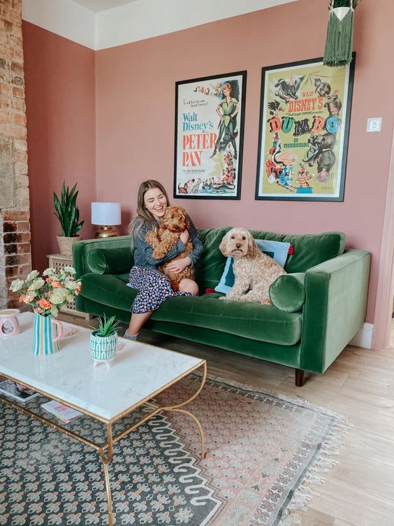 a bright living room with pink walls, a green velvet sofa, a chic coffee table and layered printed rugs plus a mini gallery wall