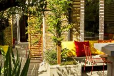 a bright outdoor space with limed oak decking, a bench with bold pillows, potted greenery and plants, red metal chairs