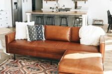 a brown leather corner sofa used as a space divider for an open layout of a kitchen and a living room