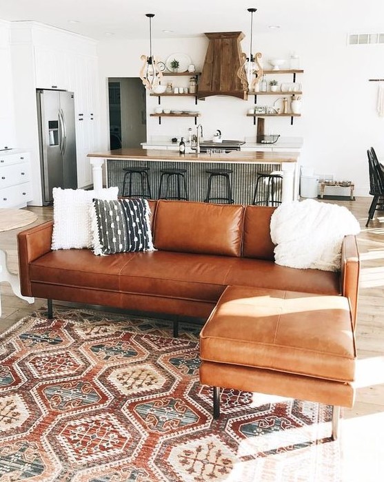 a brown leather corner sofa used as a space divider for an open layout of a kitchen and a living room