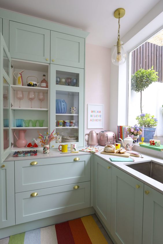 a candy-colored kitchen with mint green cabinets, pastel appliances and bright tableware, a bold striped rug