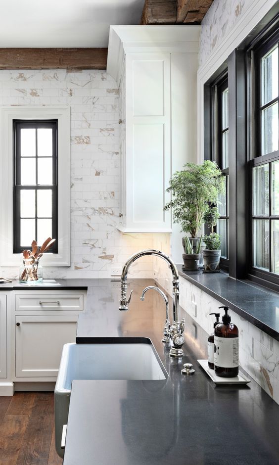 a catchy black and white kitchen with black double-hung windows, white shaker cabinets with black countertops and an elegant faucet