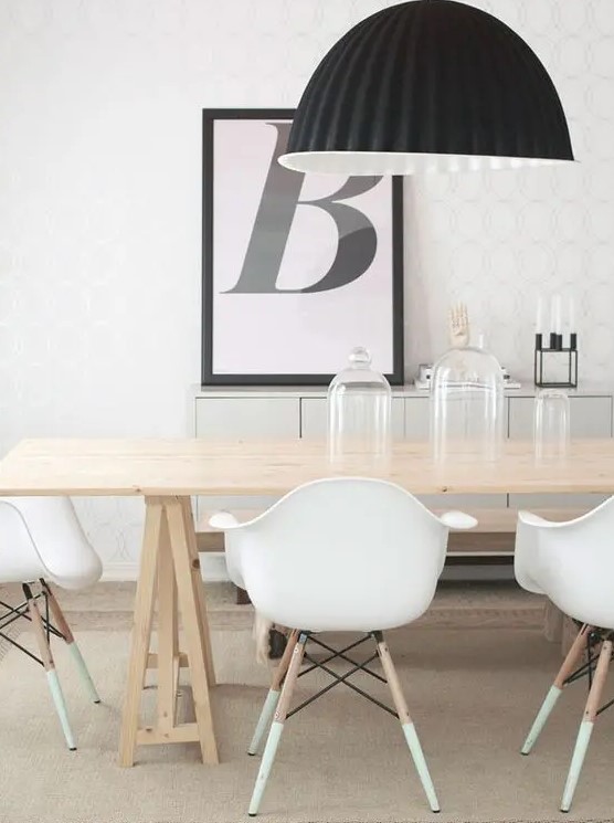 a catchy contrasting Scandinavian dining space wiht a long trestle table, white Eames chairs, a black pendant lamp and an artwork