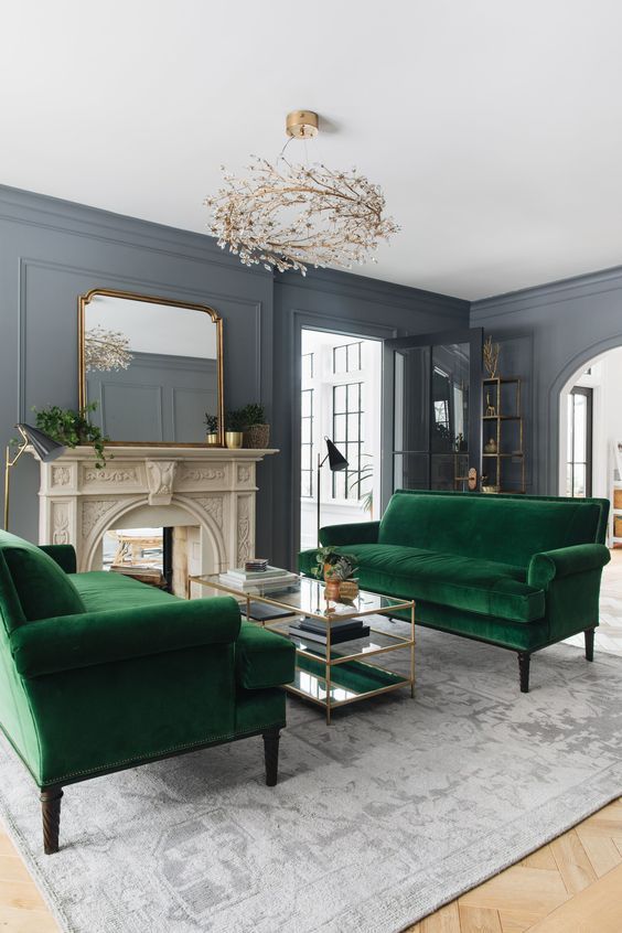 a catchy formal living room with a non-working fireplace, green velvet sofas, a tiered glass coffee table and a unique chandelier