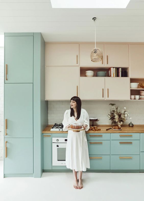 a catchy two-tone kitchen with stained and mint blue cabinets, butcherblock countertops and brass handles