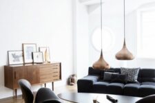 a chic Nordic living room with a black sofa and chairs, an oval coffee table, a stained sideboard and copper pendant lamps