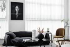 a chic Scandi living room with a black sofa and a pouf, a rust chair and a glass coffee table and some plants