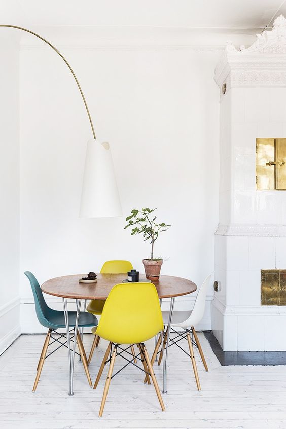 a chic Scandinavian dining space with a round table, colorful Eames chairs, a floor lamp and a hearth next to it