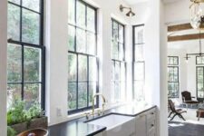 a chic black and white farmhouse kitchen with shaker cabinets, black frame double-hung windows, brass knobs and sconces