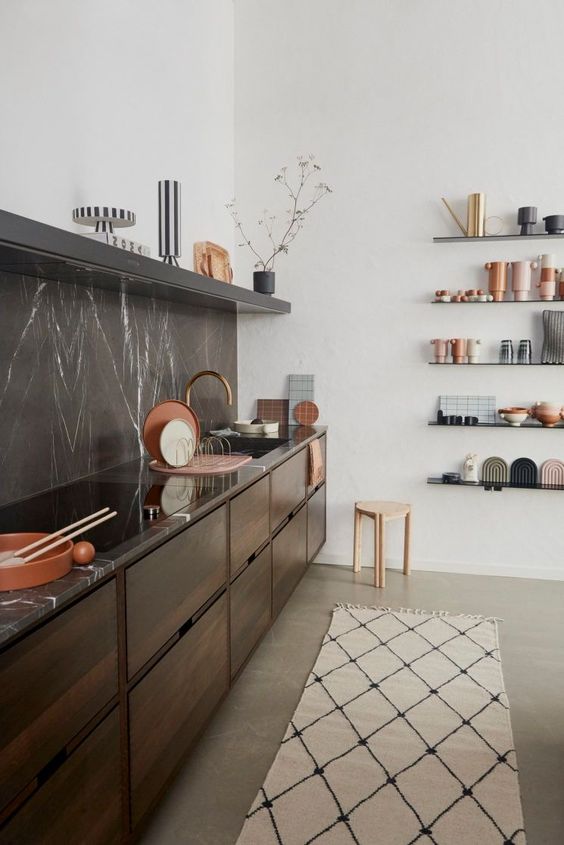a chic contemporary kitchen with dark-stained cabinets, a black soapstone backsplash and countertops, an open shelf and some pretty tableware