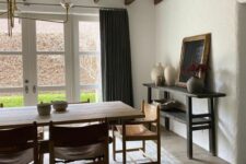 a chic earthy dining room with a glazed wall, a large stained table and leather chairs, a printed rug, a black console table and wooden beams