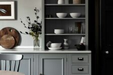 a chic grey kitchen with shaker cabinets and an open one used as a buffet to display dishes and tableware