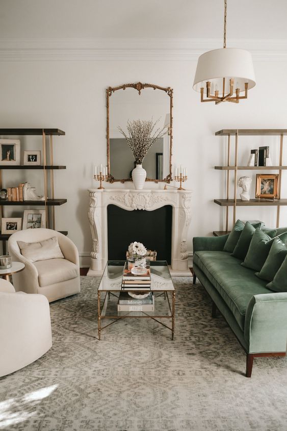 a chic living room with a French fireplace, a green sofa, neutral chairs, a tiered coffee table, a pendant lamp and bookshelves