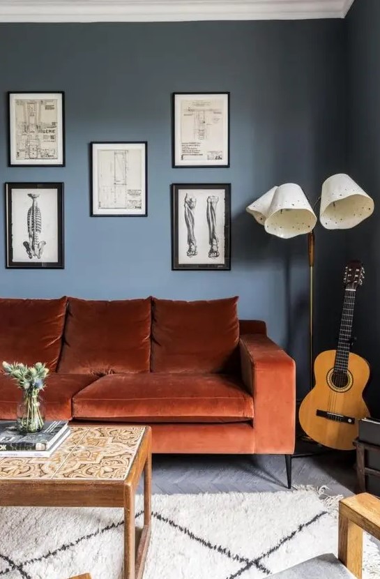 a chic living room with navy walls, a rust-colored mid-century modern sofa, a gallery wall , a floor lamp and low table with tiles is wow