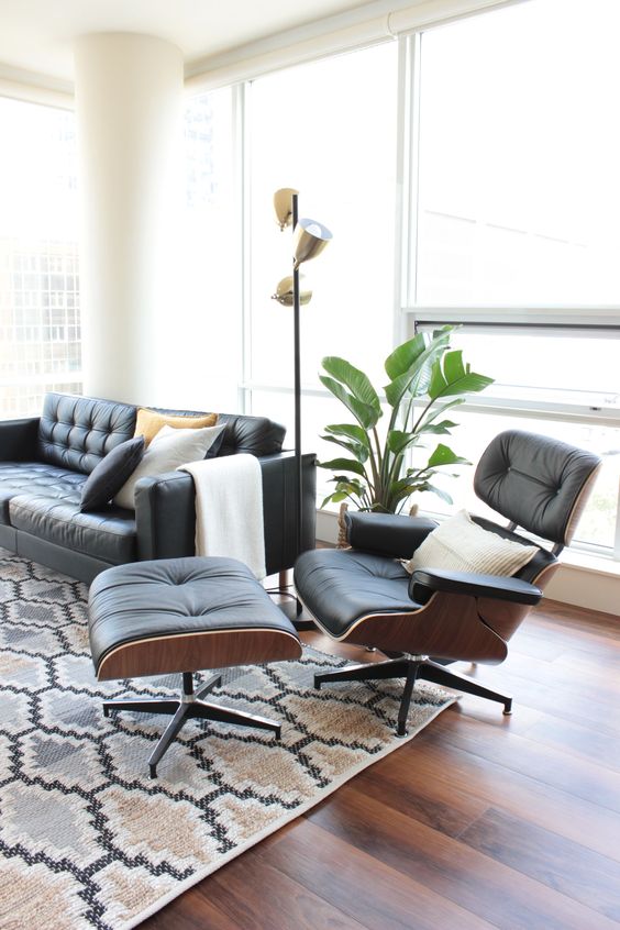 a chic mid-century modern living room with a black leather sofa and an Eames lounger and ottoman, a printed rug, a potted plant